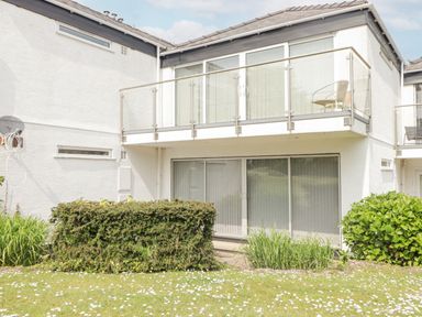 The exterior of a white two-story building with glass doors and a balcony with a chair and railing at 23 Coedrath Park in Saundersfoot