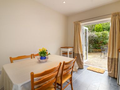 A dining room with a table and wooden chairs and a door open to a garden at Sea Breeze in Swanage