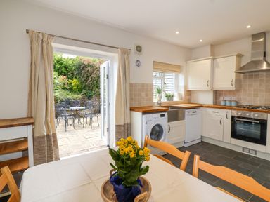 A kitchen with wooden countertops white cabinets a dining table with chairs and flowers outside seating area at Sea Breeze in Swanage