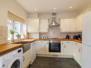 A kitchen with wooden countertops white cabinets a stainless steel oven washing machine and refrigerator at Sea Breeze in Swanage