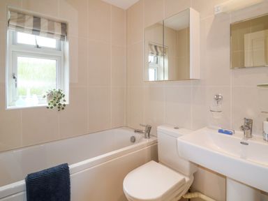 A bathroom with a bathtub a toilet a sink and a small window with a plant on the sill at Sea Breeze in Swanage