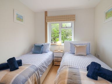 A bedroom with two single beds with checked bedding a small table with a lamp between the beds and a window with a checked blind at Sea Breeze Swanage