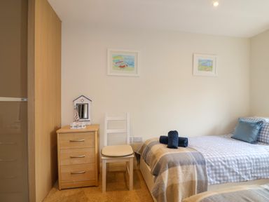 A bedroom with a single bed blue check bedding a bedside cabinet and a white chair at Sea Breeze in Swanage