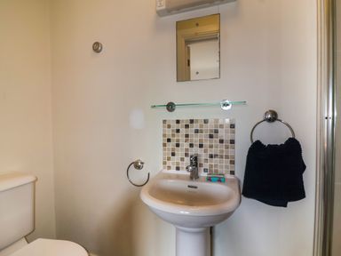 A bathroom with a white pedestal sink and a small mirror above it at Sea Breeze in Swanage