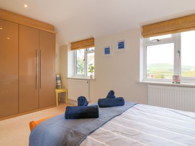 A bedroom with a bed, blue rolled towels, brown wardrobe, yellow chair, and windows with views at Sea Breeze in Swanage