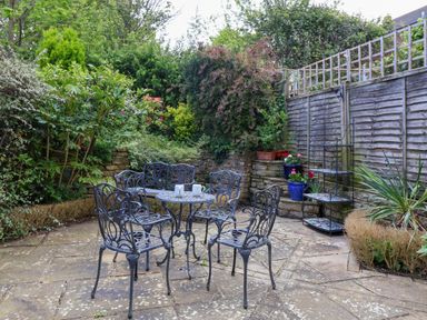 An outdoor patio with a metal table and chairs surrounded by plants and a wooden fence at Sea Breeze in Swanage
