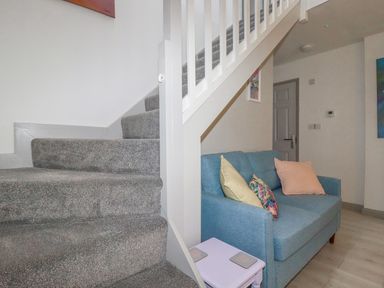 A stairway with grey carpet leading up and a blue sofa with pillows under the stairs at Rainbow Lodge in St Tudy