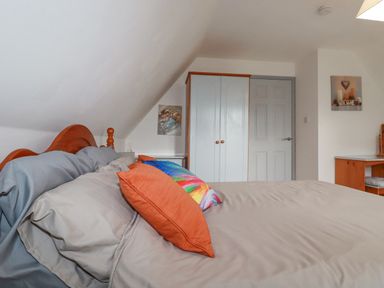 A bedroom with a bed with colorful pillows a wardrobe a door and a desk at Rainbow Lodge in St Tudy