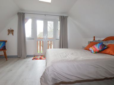 A bedroom with a bed orange pillows a chair with a colorful cushion and a door leading outside at Rainbow Lodge in St Tudy
