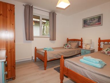 A bedroom with two single wooden beds a nightstand with a lamp a window with curtains and a wardrobe at Rainbow Lodge in St Tudy