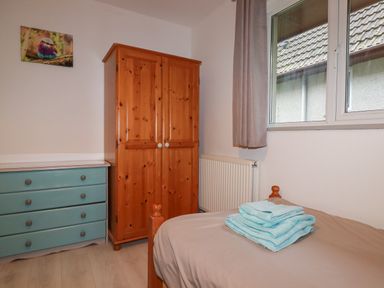 A bedroom with a wooden wardrobe a blue chest of drawers a bed with folded towels and a window with curtains at Rainbow Lodge in St Tudy
