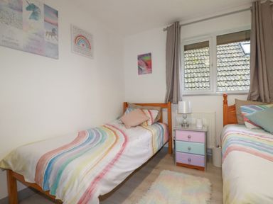 A bedroom with two single beds with rainbow striped bedding a small pastel colored nightstand a lamp and framed pictures on the wall at Rainbow Lodge in St Tudy