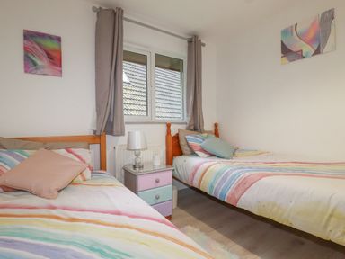 A bedroom with two single beds a nightstand lamp and window with curtains at Rainbow Lodge in St Tudy