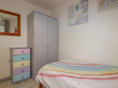 A bedroom with a bed with a rainbow striped duvet a wardrobe a chest of drawers with pastel colors and a wall mirror at Rainbow Lodge in St Tudy
