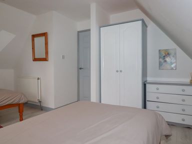 A bedroom with two beds a white wardrobe a white chest of drawers a wooden framed mirror and a painting on the wall at Rainbow Lodge in St Tudy