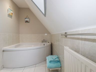 A bathroom with a corner bathtub two pictures on the wall a radiator and folded towels on a rack at Rainbow Lodge in St Tudy