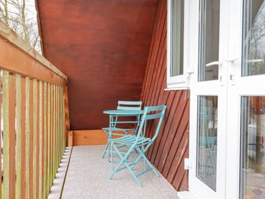 A balcony with a turquoise table and two chairs next to a white door at Rainbow Lodge in St Tudy