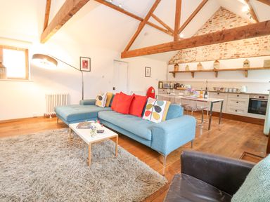 An open plan living room and kitchen with blue sofa wooden beams and a dining table at Packway Barn in Halesworth
