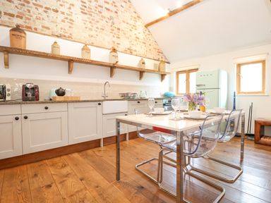 A kitchen with a dining table, transparent chairs, exposed brick wall, and a light blue fridge at Packway Barn in Halesworth