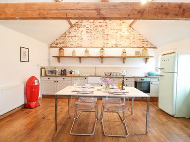A kitchen with a dining table set for four in front of a brick wall with wooden shelf and kitchen appliances at Packway Barn in Halesworth