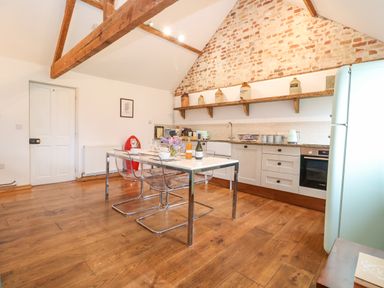 A kitchen with wooden floor a dining table with transparent chairs and a brick wall at Packway Barn in Halesworth