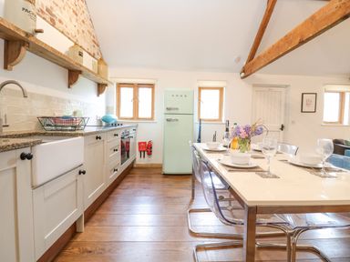 A kitchen with white cabinets a green smeg fridge and a dining table set for four at Packway Barn in Halesworth