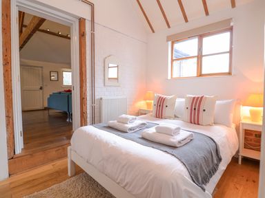 A bedroom with a white bed with striped pillows and folded towels on top of a gray runner at Packway Barn in Halesworth