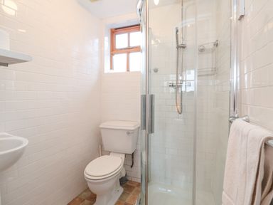 A bathroom with a toilet a corner shower with glass doors a towel on a rack and a small window at Packway Barn in Halesworth