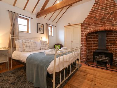 A bedroom with a metal bed frame two windows a brick fireplace a wardrobe and a chair at Packway Barn in Halesworth