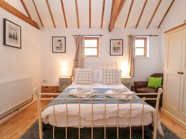 A bedroom with a double bed two bedside tables two lamps an armchair and a wardrobe at Packway Barn in Halesworth