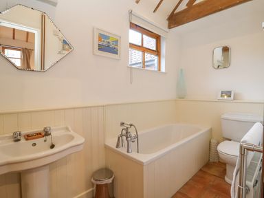 A bathroom with a sink a bathtub a toilet wooden beams and mirrors at Packway Barn in Halesworth
