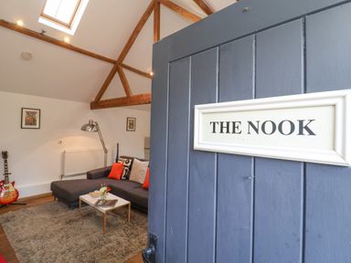 A seating area with a gray sofa orange cushions coffee table and a guitar near a lamp at The Nook in Chediston near Halesworth