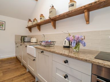 A kitchen with white cabinets a wooden floor stone countertop and ceramic jugs on a wooden shelf at The Nook in Chediston near Halesworth