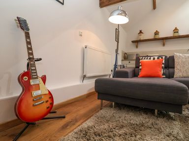 A living room with a guitar on a stand a gray sofa with cushions a floor lamp and a wooden floor at The Nook in Chediston near Halesworth