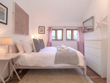 A bedroom with a double bed bedside table lamp window with purple curtains and a white chest of drawers at The Nook in Chediston near Halesworth