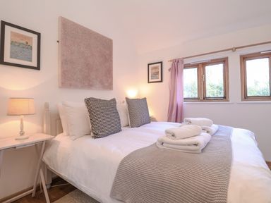 A bedroom with a bed with white linens and folded towels two framed pictures on the walls and three windows with curtains at The Nook in Chediston near Halesworth
