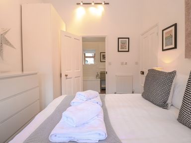 A bedroom with a bed with folded towels on a blanket a dresser a wardrobe and a doorway leading to a bathroom at The Nook in Chediston near Halesworth