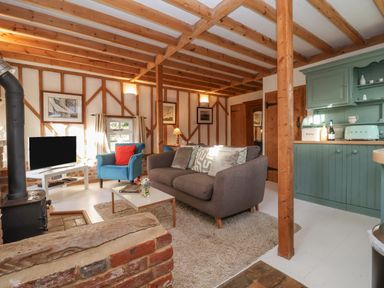 A living room with a grey sofa blue armchair white coffee table and green kitchen cabinets at Twosome in Chediston near Halesworth