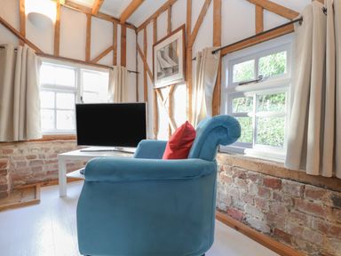 A blue armchair with a red cushion next to a white table with a television in a room with exposed wooden beams and brick walls at Twosome in Chediston near Halesworth