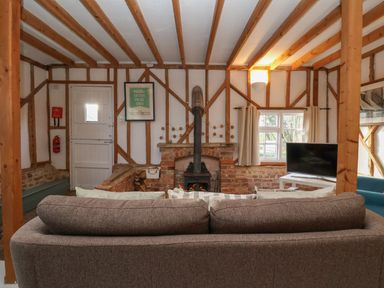 A living room with a gray sofa a wood burning stove a television and exposed wooden beams at Twosome in Chediston near Halesworth