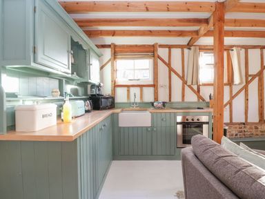 A kitchen with green cabinets wooden beams a white sink and a gray sofa at Twosome in Chediston near Halesworth
