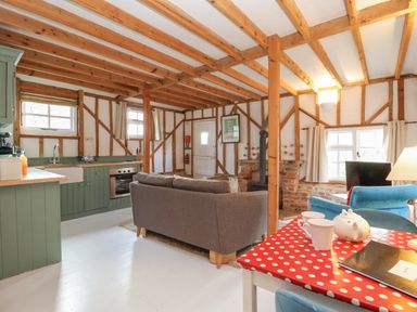 An open kitchen and living area with wooden beams a grey sofa and a red polka dot tablecloth at Twosome in Chediston near Halesworth