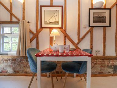 A dining area with a red polka dot tablecloth on a white table blue chairs a teapot mugs and framed pictures on the wall at Twosome in Chediston near Halesworth