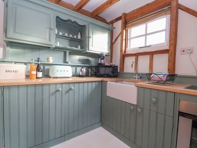 A kitchen with green cabinets a white sink and wooden countertops at Twosome in Chediston near Halesworth