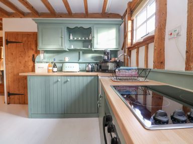 A kitchen with green cabinets wooden beams and a stovetop at Twosome in Chediston near Halesworth