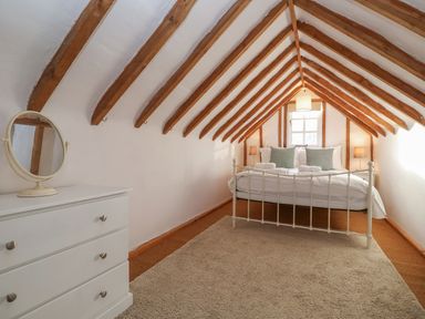 A bedroom with a bed side tables and a dresser with a mirror under a ceiling with wooden beams at Twosome in Chediston near Halesworth