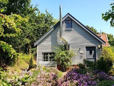 A small house with gray siding surrounded by trees and purple flowering plants at Twosome in Chediston near Halesworth