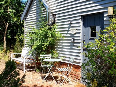 A white bench and two chairs with a round table outside a building with blue door and white siding at Twosome in Chediston near Halesworth