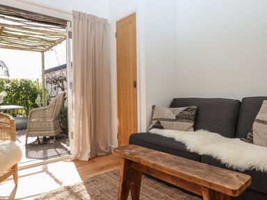 A living room with a dark sofa and wooden coffee table next to an open door leading to an outdoor seating area at The Apple Shed in Upexe near Silverton