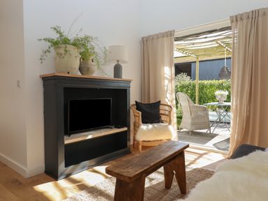A living room with a black TV cabinet holding a TV and lamps beside a chair and wooden bench by a sliding door at The Apple Shed in Upexe near Silverton